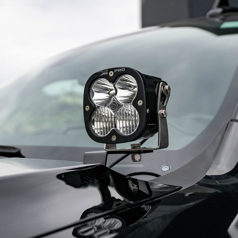 Baja Designs XL Pro A-Pillar Light Kit on a vehicle: A black XL Pro pod with a clear lens mounted on an A-pillar bracket beside the hood of a dark truck