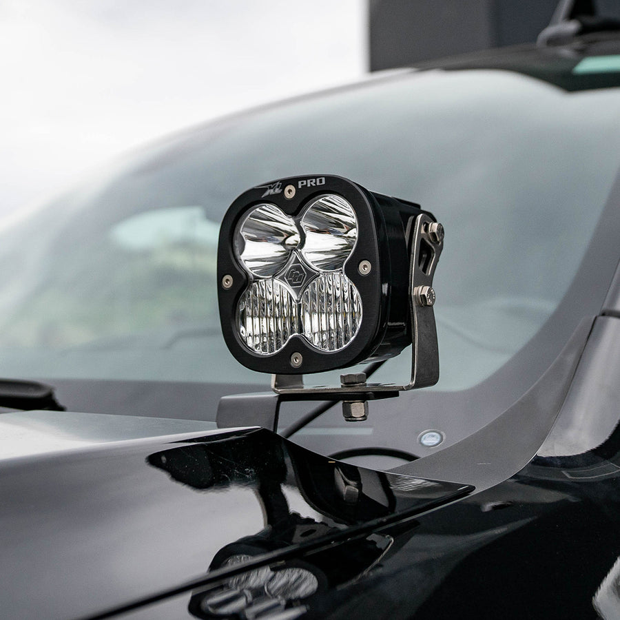 Baja Designs XL Pro A-Pillar Light Kit on a vehicle: A black XL Pro pod with a clear lens mounted on an A-pillar bracket beside the hood of a dark truck