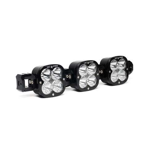 Baja Designs XL Pro Linkable LED Light Bar, whole product on a studio background: A 3-light black XL Pro Linkable LED light bar with clear lenses and end mounting blocks, shown at a close front three-quarter angle on a white background