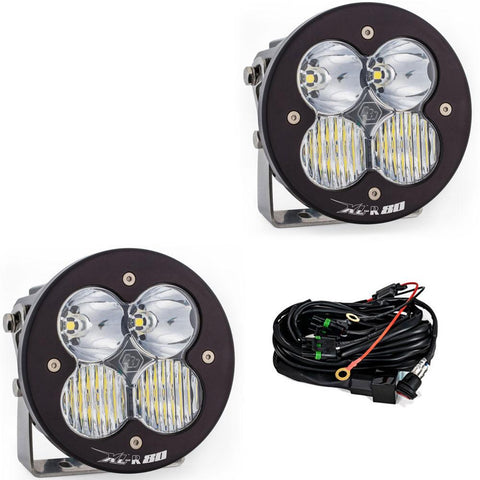 Baja Designs XL-R 80 LED Auxiliary Light Pod Pair, whole product on a studio background: A pair of Baja Designs round XL-R 80 pods with clear lenses shown on a white background beside the wiring harness