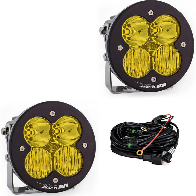 Baja Designs XL-R 80 LED Auxiliary Light Pod Pair, whole product on a studio background: A pair of Baja Designs round XL-R 80 pods with amber lenses shown on a white background beside the wiring harness