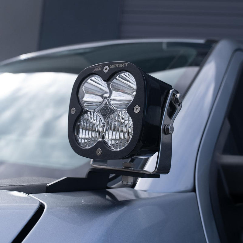 Baja Designs XL Sport A-Pillar Light Kit on a vehicle: A Baja Designs XL Sport LED pod mounted on an A-pillar bracket beside the windshield of a gray truck