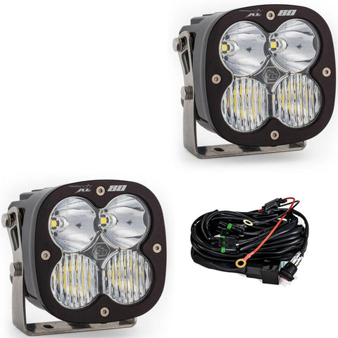Baja Designs XL80 LED Auxiliary Light Pod Pair, whole product on a studio background: A pair of Baja Designs XL 80 pods with clear lenses shown on a white background beside the wiring harness