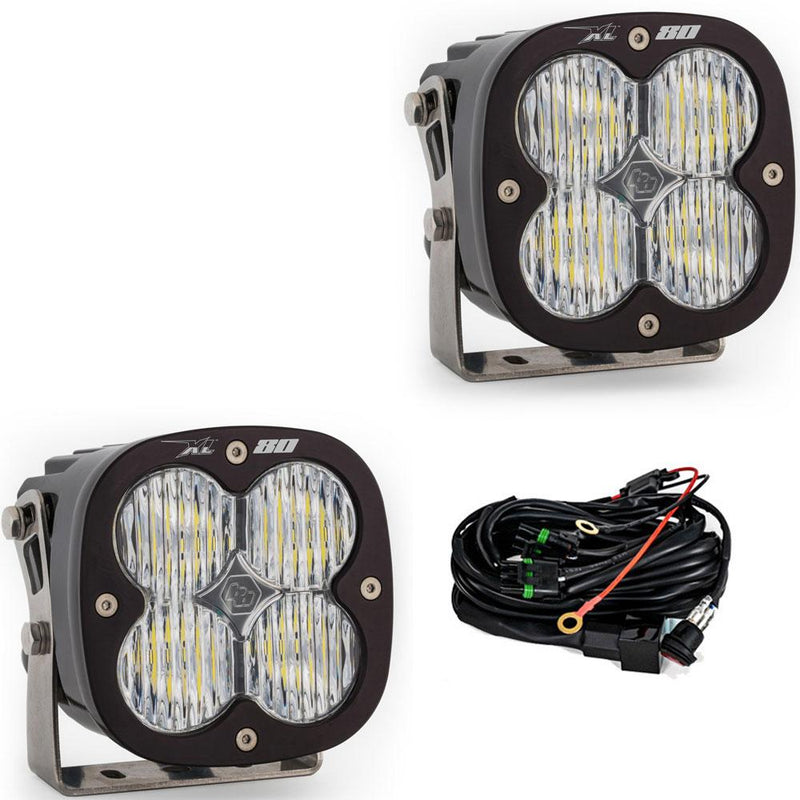Baja Designs XL80 LED Auxiliary Light Pod Pair, whole product on a studio background: A pair of Baja Designs XL 80 pods with clear lenses shown on a white background beside the wiring harness