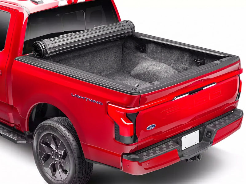 BAK Revolver X4s tonneau cover fully rolled up into its canister at the cab of a red Ford F-150 Lightning, exposing the empty carpeted truck bed