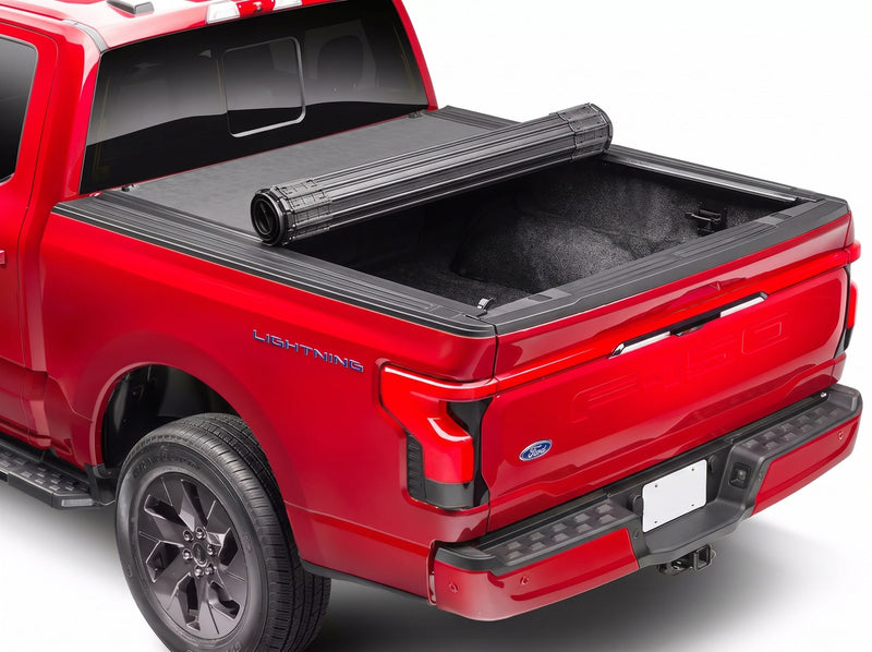 BAK Revolver X4s tonneau cover partially rolled open on a red Ford F-150 Lightning, with the black slatted cover half retracted toward the cab and the rear of the bed uncovered