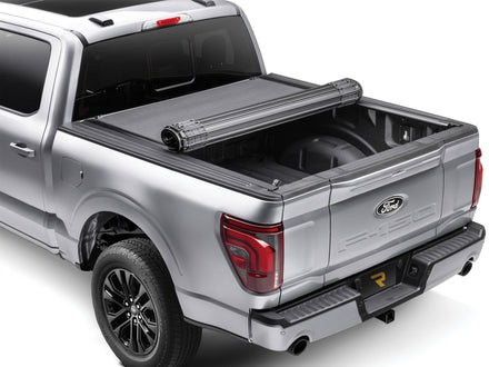 BAK Revolver X4s hard roll-up tonneau cover partly rolled toward the cab on a silver pickup, rear three-quarter view