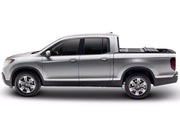 BAKFlip F1 hard folding tonneau cover folded flat and stacked at the front of the bed on a silver Honda Ridgeline, side profile on a white background