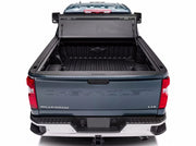 Straight-on rear view of a dark blue Chevrolet Silverado with the BAKFlip G2 tonneau cover panels folded and stacked upright at the cab, exposing the empty black bed floor