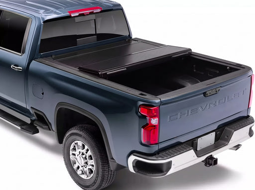 BAKFlip G2 hard folding tonneau cover in black folded forward against the cab of a dark blue Chevrolet Silverado, shown from a rear three-quarter angle with the truck bed open