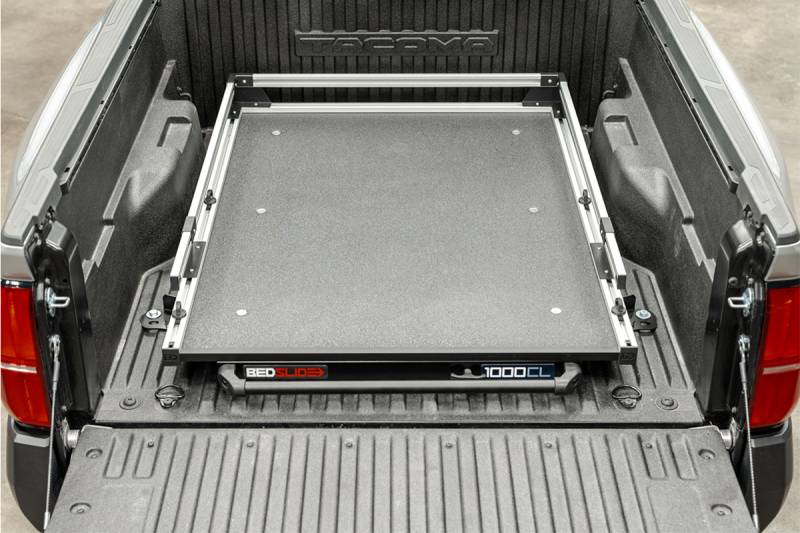 BEDSLIDE 1000 Classic cargo slide in Silver finish installed in a Toyota Tacoma bed with the 1000CL badge visible