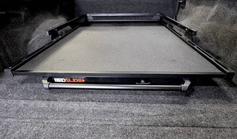 BEDSLIDE cargo slide in Black Edition finish photographed low from the tailgate showing the full width grab bar. BEDSLIDE uses this Black Edition photograph across its Classic and Heavy Duty ranges and the front rail carries no model badge, so the frame does not identify which range it shows.