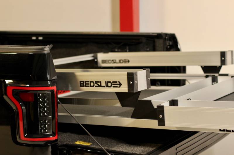 Close-up of a silver BEDSLIDE BEDBIN mounted on a slide deck, showing the aluminum extrusion and the BEDSLIDE decal