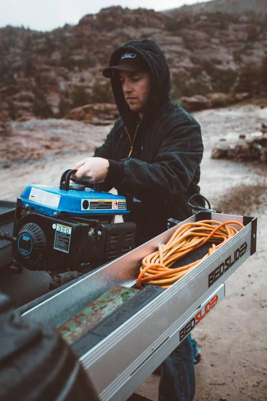 Person loading an extension cord into a silver Side Kix bin on a truck tailgate outdoors