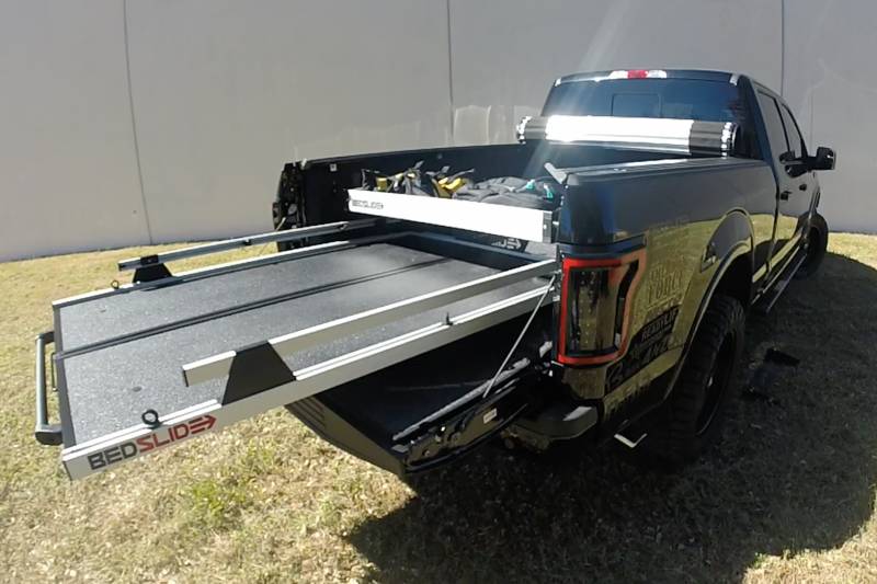 Silver upper BEDBIN tray mounted above an extended BEDSLIDE deck on a black pickup, photographed outdoors.