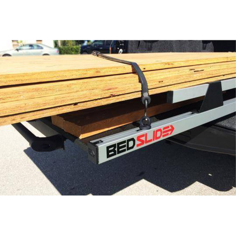 BEDSLIDE D-ring tie-down in use on the BEDTRAX track of a silver slide deck, with a strap over a load of lumber