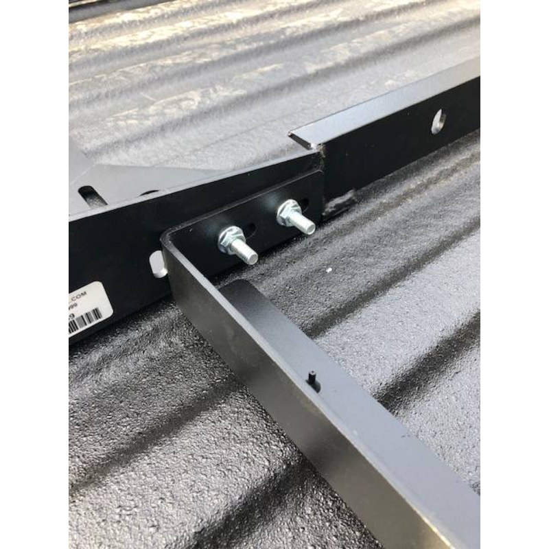 Close-up of a BEDSLIDE no-drill mounting bracket bolted down inside a spray-lined truck bed, showing the two studs and the bracket arm running across the bed floor
