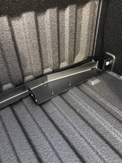 Close-up of a BEDSLIDE no-drill bracket arm running across the ribbed floor of a spray-lined truck bed and fastened at the bed side