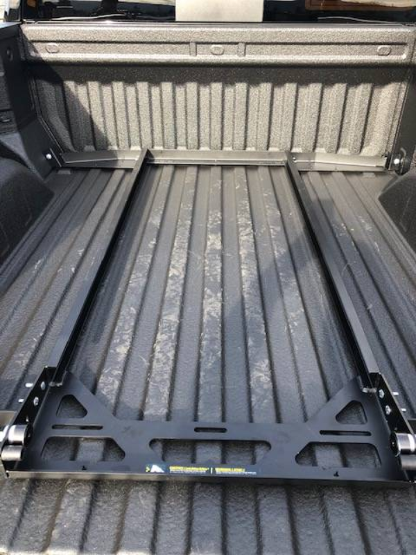 BEDSLIDE no-drill mounting brackets fitted across the floor of a full-size spray-lined truck bed, viewed from the tailgate before the slide goes on