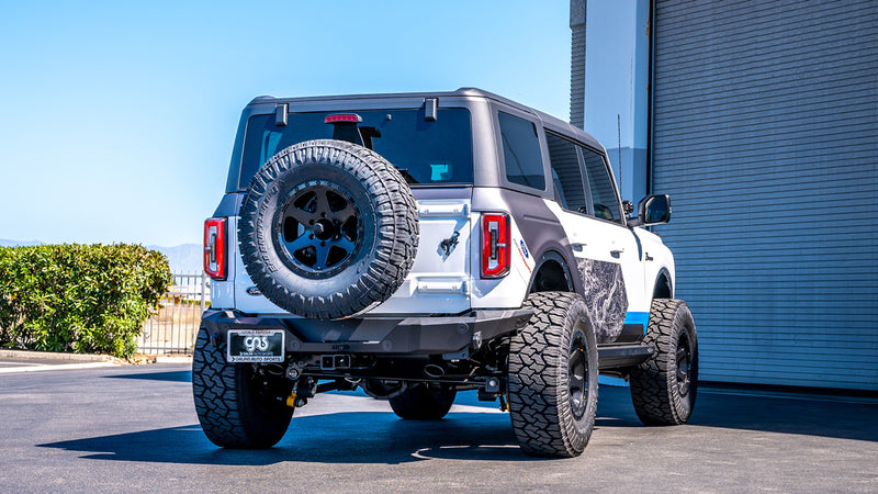 Borla ATAK Axle-Back Exhaust System installed on a Ford Bronco 4-door: A white four-door Ford Bronco seen squarely from the rear in front of a building; the exhaust tip finish is not visible