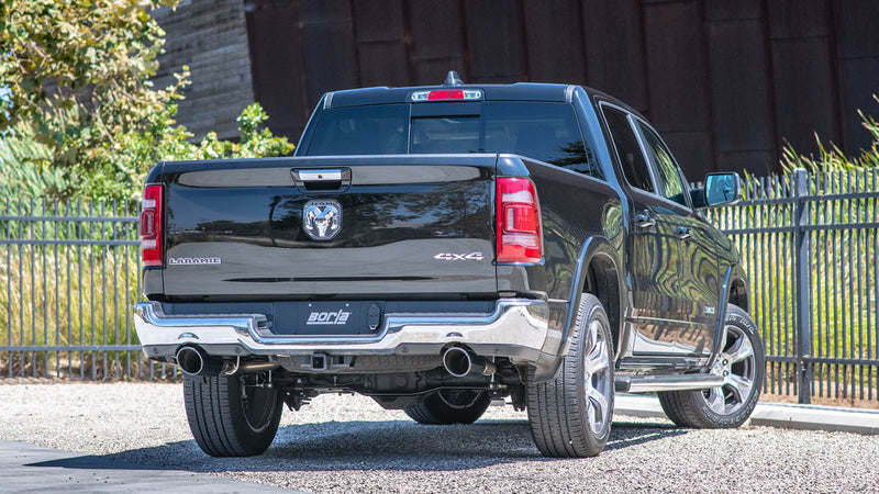 Borla ATAK Cat-Back Exhaust System installed on a Ram 1500: A black Ram 1500 crew cab parked by a fence, seen from the rear with dual exhaust tips and a Borla plate