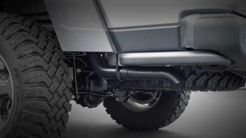 Borla ATAK Cat-Back Exhaust System on a vehicle: an underbody view of a black coated exhaust tail pipe routed behind the rear tire of an off-road vehicle