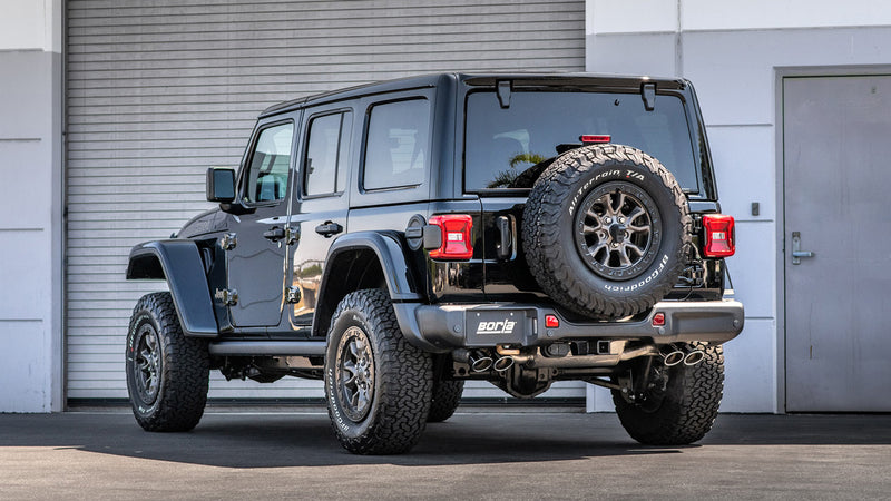 Borla ATAK Cat-Back Exhaust System installed on a Jeep Wrangler: black Jeep Wrangler Unlimited seen from the rear quarter in front of a garage door, with exhaust tips under the rear bumper