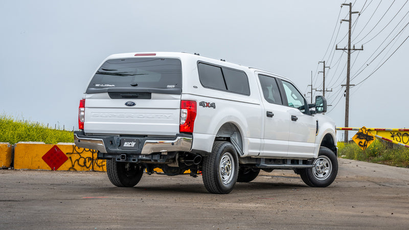 Borla ATAK Cat-Back Exhaust System installed on a Ford F-250 Super Duty: white Ford F-250 Super Duty crew cab with a camper shell, seen from the rear quarter on a roadside