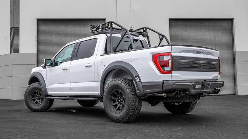 Borla ATAK Mid-Section Exhaust System installed on a Ford F-150 Raptor: white Ford F-150 Raptor with a cargo roll bar parked in front of garage doors, rear three-quarter view
