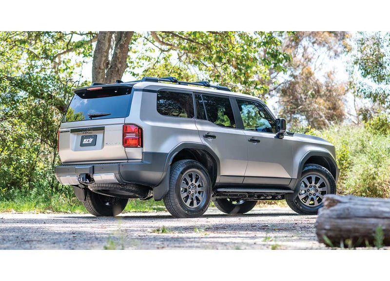 Borla S-Type Cat-Back Exhaust System installed on a Toyota Land Cruiser: rear three-quarter view of a silver Toyota Land Cruiser with a Borla plate parked on a tree-lined dirt road