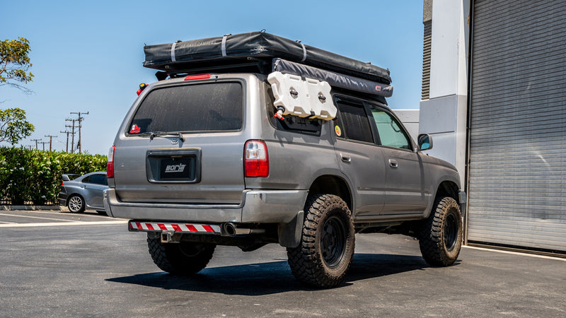 Borla Touring Cat-Back Exhaust System installed on a Toyota 4Runner: lifted silver Toyota 4Runner with a roof-top tent and Borla license plate parked beside a building