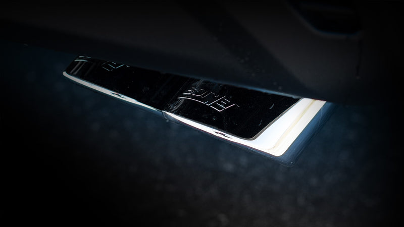 Close-up of the Borla Touring Cat-Back Exhaust System: low-light close-up of a mirror-finish angle-cut exhaust tip with an etched Borla logo; finish reads dark under the lighting