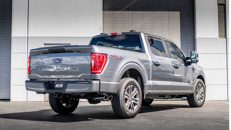 Borla Touring Cat-Back Exhaust System installed on a Ford F-150: rear three-quarter view of a gray Ford F-150 with dual Borla tips by a warehouse