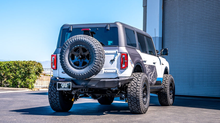 Axle-Back Exhaust Systems by Borla: A white four-door Ford Bronco seen squarely from the rear in front of a building; the exhaust tip finish is not visible.