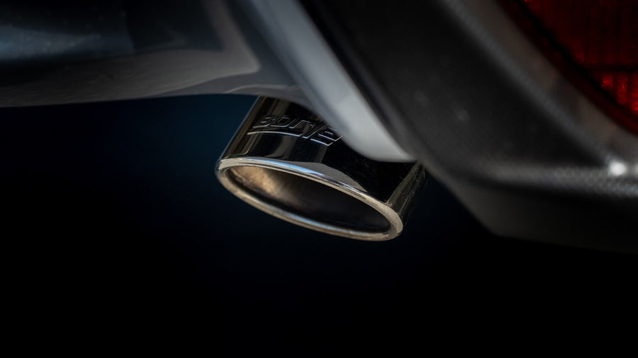 Axle-Back Exhaust Systems by Borla: A polished exhaust tip with an etched Borla logo under a dark vehicle bumper against a black background.