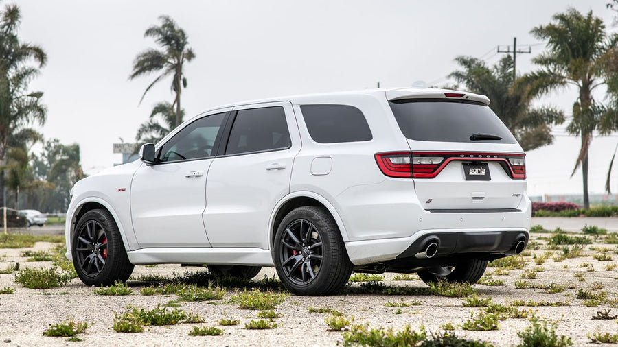 Cat-Back Exhaust Systems by Borla: A white Dodge Durango SRT parked on gravel by palm trees, seen from the rear quarter with dual exhaust tips.
