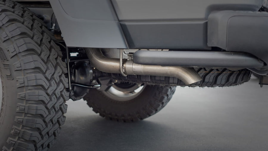 Cat-Back Exhaust Systems by Borla: An underbody view of a stainless exhaust tail pipe routed behind the rear tire of an off-road vehicle.