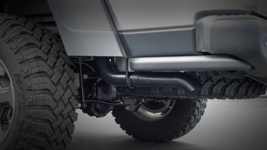 Cat-Back Exhaust Systems by Borla: An underbody view of a black coated exhaust tail pipe routed behind the rear tire of an off-road vehicle.