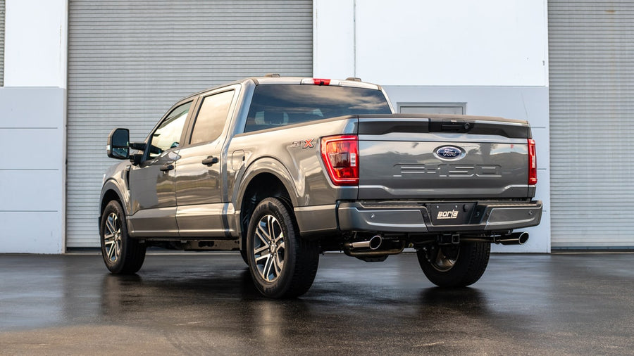 Cat-Back Exhaust Systems by Borla: Rear three-quarter view of a gray Ford F-150 with a Borla exhaust tip on a wet pad by a warehouse.