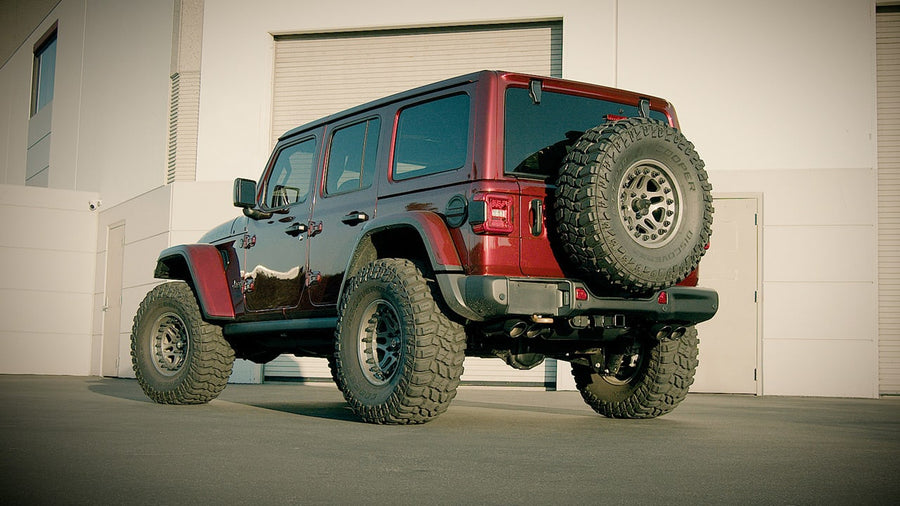 Cat-Back Exhaust Systems by Borla: Red Jeep Wrangler Unlimited on large mud tires seen from the rear quarter with dark dual exhaust tips under the rear bumper.