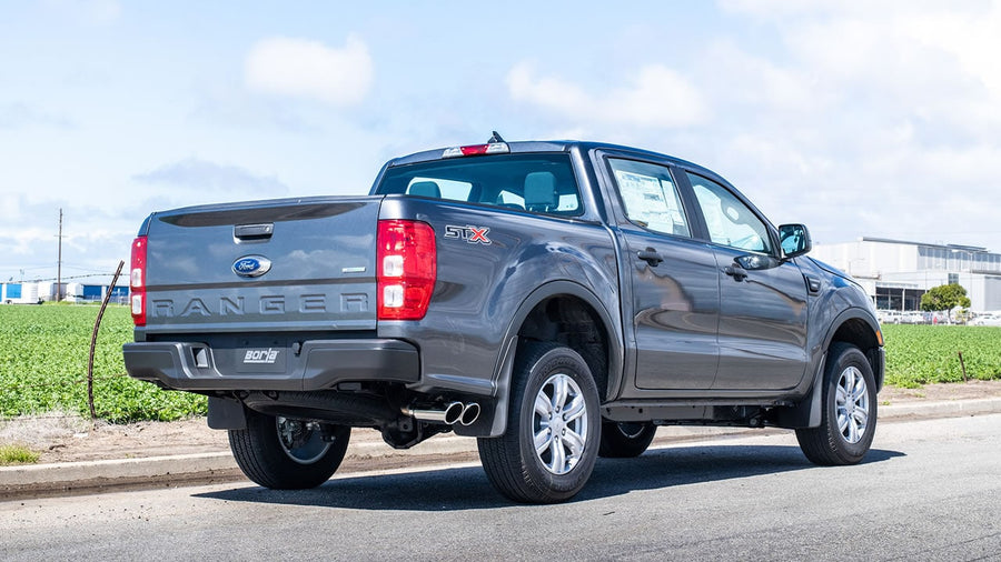 Cat-Back Exhaust Systems by Borla: A gray Ford Ranger crew cab parked by a field, rear quarter view showing twin exhaust tips exiting ahead of the rear wheel.