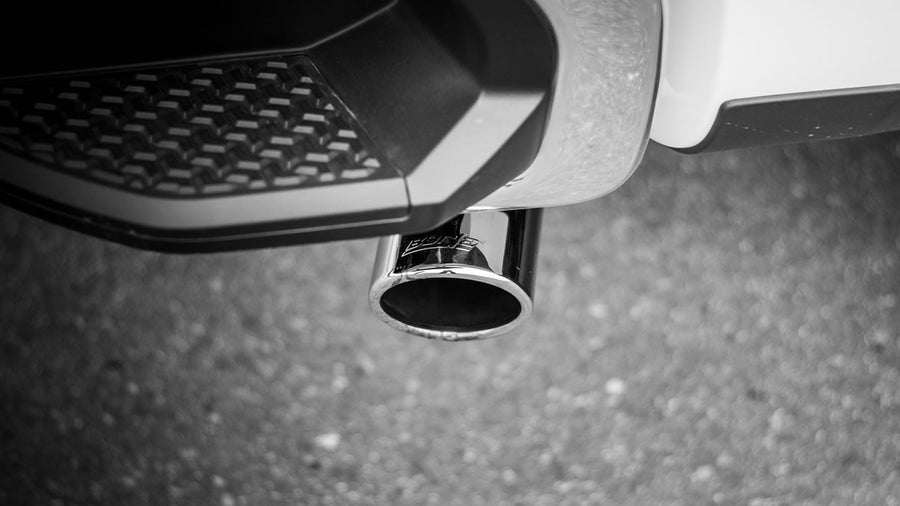 Cat-Back Exhaust Systems by Borla: Black and white close-up of a single polished exhaust tip with etched BORLA lettering under a white pickup bumper step.