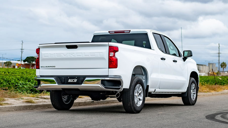 Cat-Back Exhaust Systems by Borla: A white Chevrolet Silverado double cab parked on a road, rear quarter view showing exhaust tips under the rear bumper.