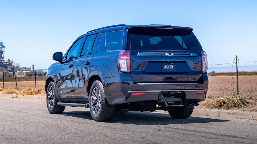 Cat-Back Exhaust Systems by Borla: Rear three-quarter view of a dark blue Chevrolet Tahoe parked on a rural road with exhaust tips under the rear bumper.