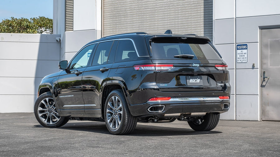 Cat-Back Exhaust Systems by Borla: A black Jeep Grand Cherokee parked beside a white building, seen from the rear three-quarter.
