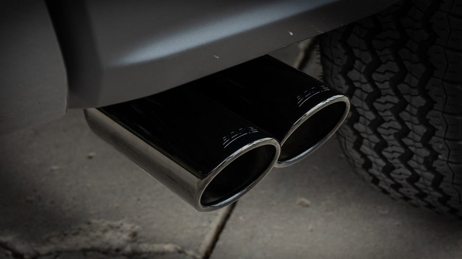 Cat-Back Exhaust Systems by Borla: Close view of dual black chrome tips with etched Borla lettering exiting ahead of a rear tire.