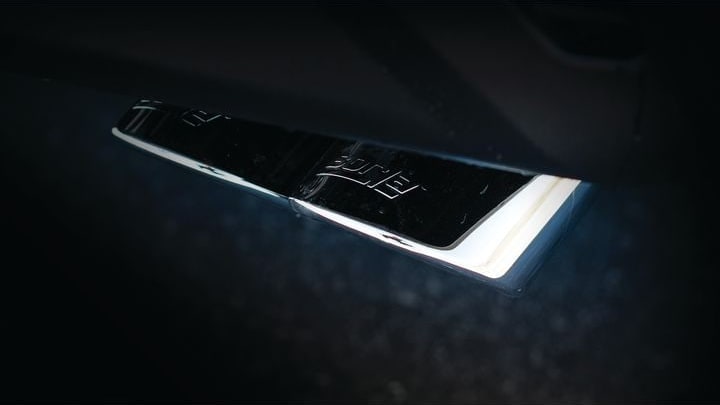Cat-Back Exhaust Systems by Borla: Close-up of a mirror-finish exhaust tip with etched Borla script, lit against a dark background beneath a vehicle.