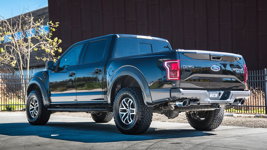 Mid-Section Exhaust Systems by Borla: Black Ford F-150 Raptor rear three-quarter view with polished exhaust tips exiting ahead of both rear tires.