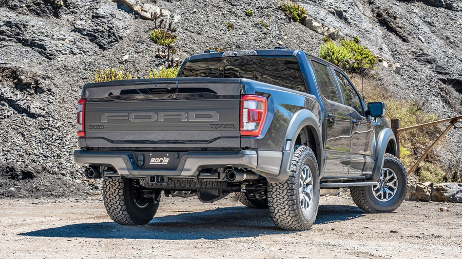 Tail Pipe & Connecting Pipe Kits by Borla: A gray Ford F-150 Raptor with FORD embossed tailgate is parked on a rocky road with exhaust tips at both rear wheels.