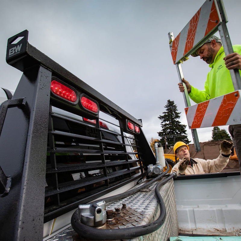 B&W cab protector fitted to a white work truck on a jobsite, with a crew loading barricades into the bed